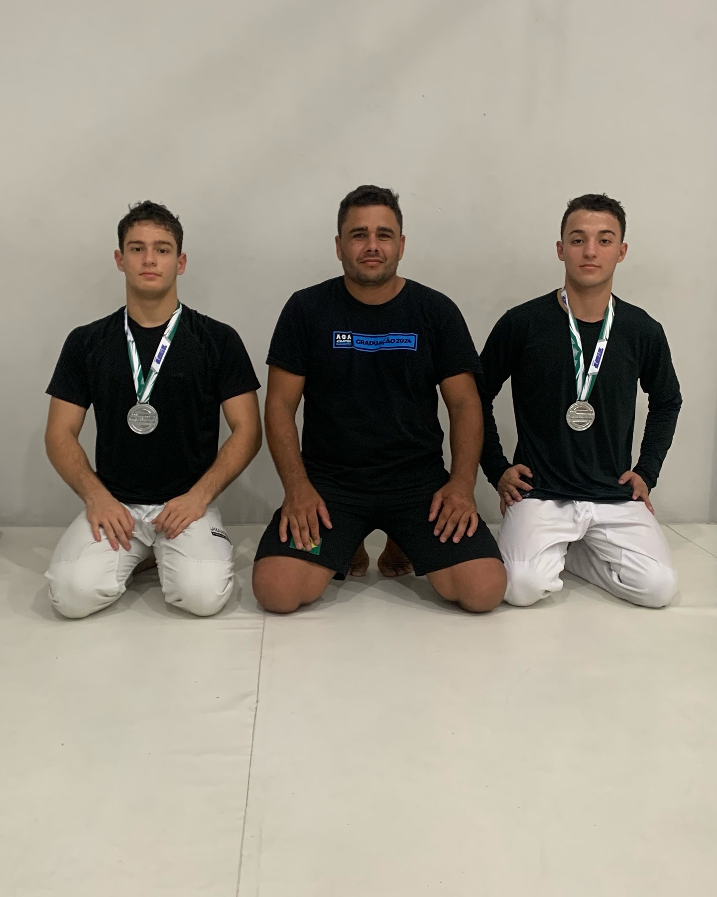 Três atletas do Dojo Nato ajoelhados no tatame com medalhas