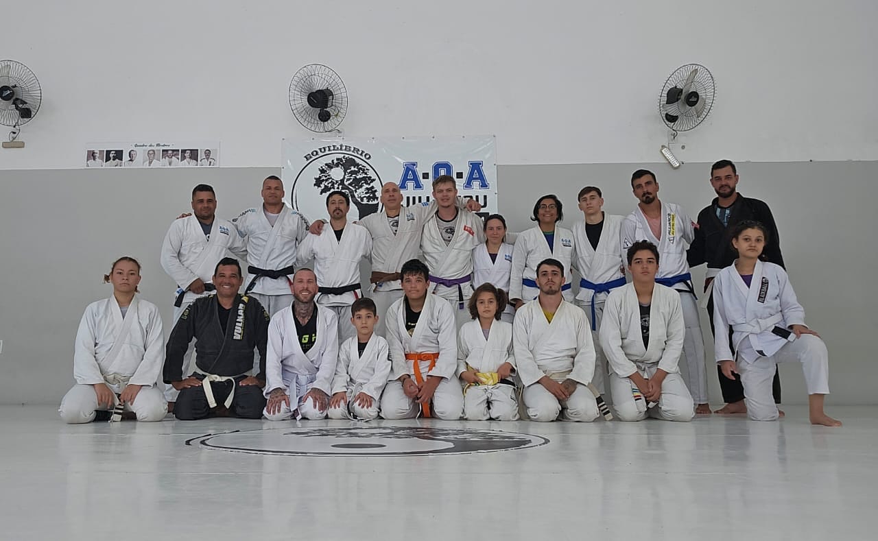 Alunos e professores do Dojo Nato de kimono, sentados e em pé no tatame